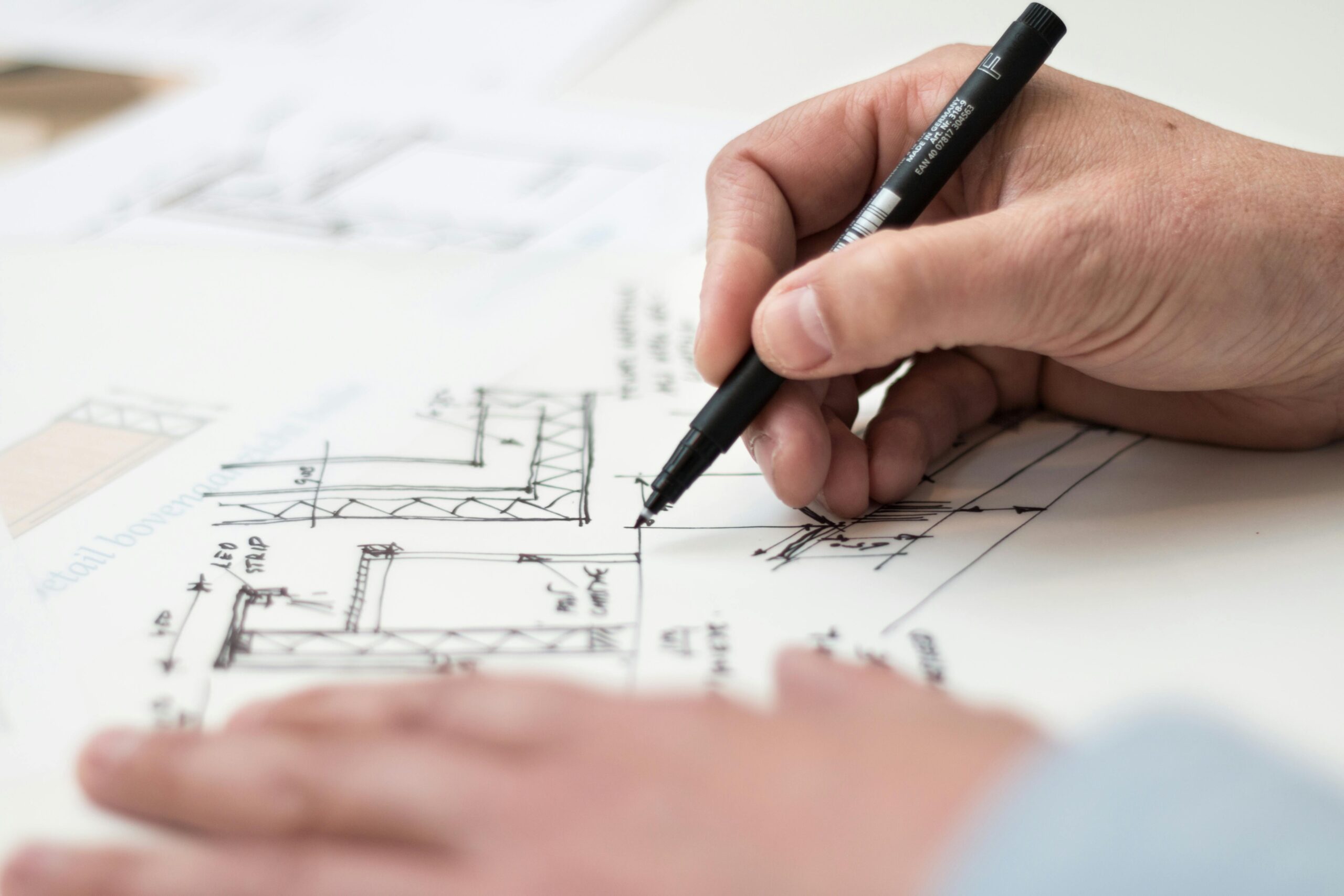 Close-up of hand drawing intricate technical designs on blueprint with pen.