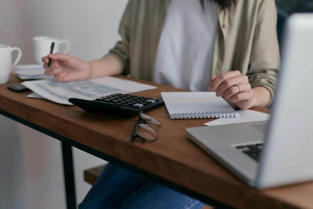 A woman creating an estimate, using a laptop and calculator on a wooden desk.